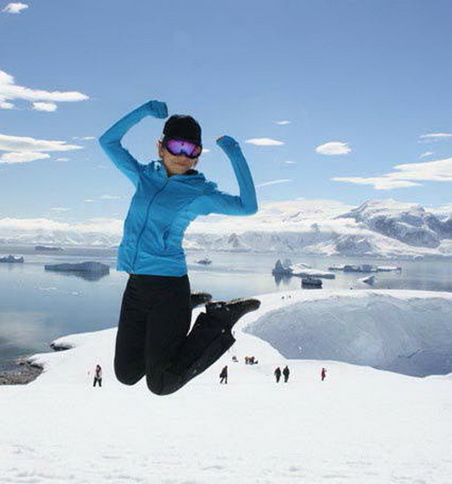 une femme saute devant la caméra avec l'antarctique en arrière plan