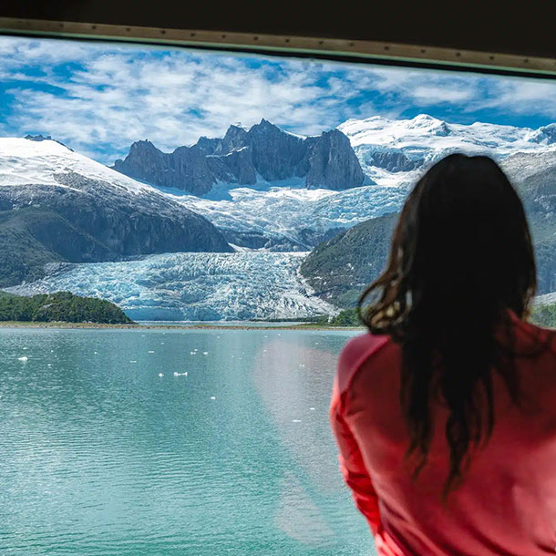 une passagère regarde par la fenêtre panoramique de sa cabine le paysage du glacier Pia et des montagnes envirronnantes