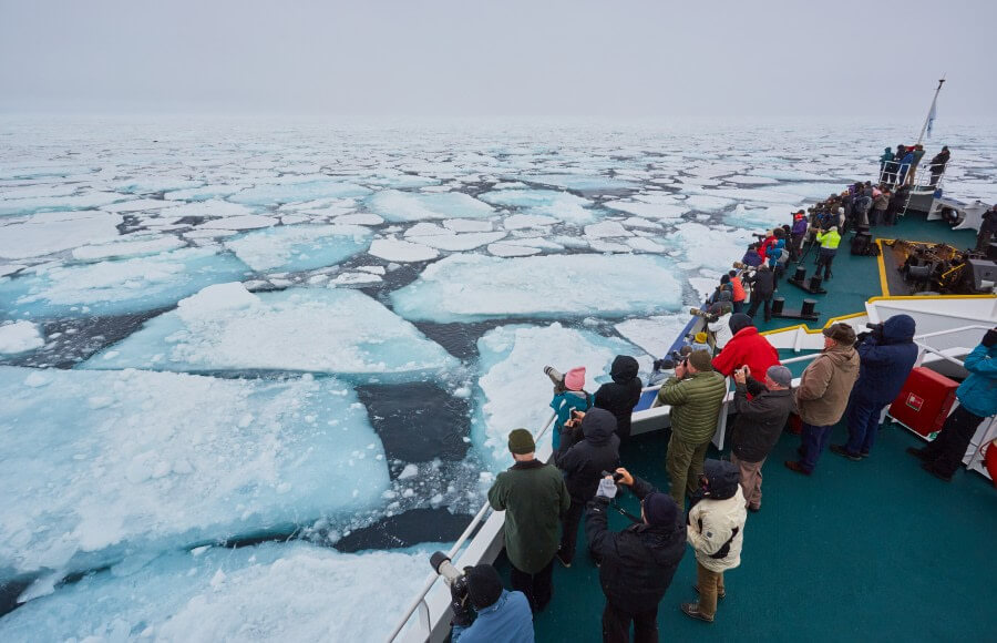 un bateau polaire fend la glace avec les passagers qui observent depuis la proue