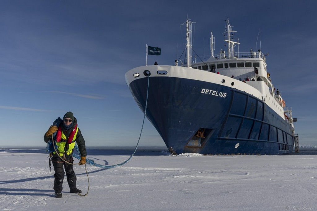 un homme sur la banquise tient l'amarre du bateau ortelius